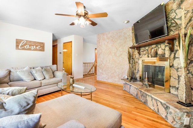 living room featuring hardwood / wood-style floors, ceiling fan, and a stone fireplace