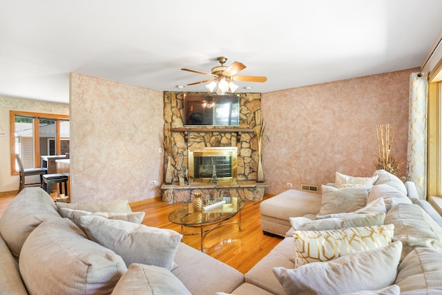 living room with a stone fireplace, ceiling fan, and wood-type flooring