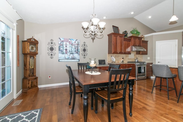 dining area featuring vaulted ceiling, hardwood / wood-style floors, and an inviting chandelier