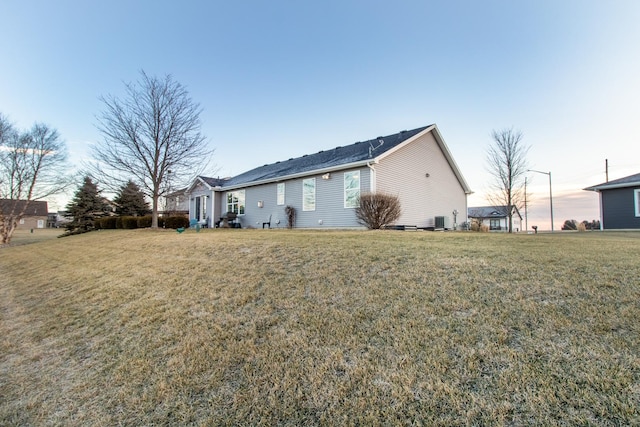 back house at dusk with a lawn and central air condition unit