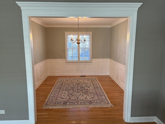 unfurnished dining area featuring a chandelier, wood-type flooring, and ornamental molding