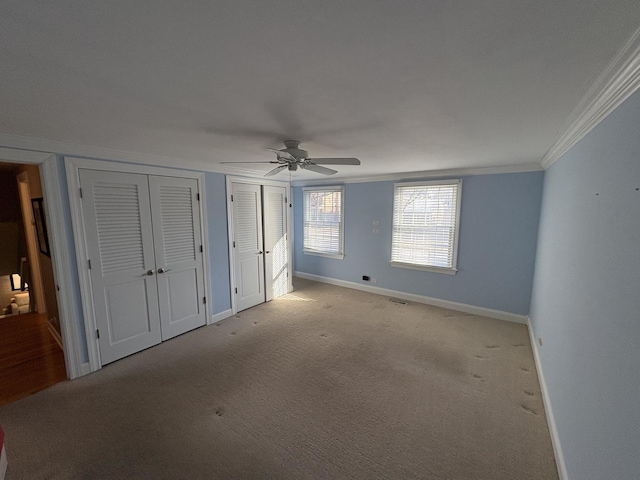 unfurnished bedroom with ceiling fan, light colored carpet, two closets, and ornamental molding