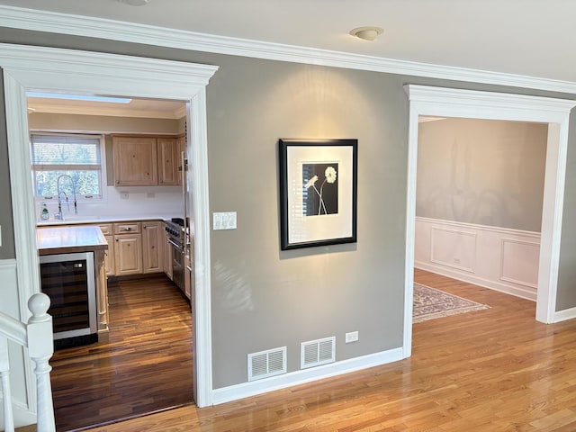 kitchen featuring light brown cabinetry, ornamental molding, sink, light hardwood / wood-style flooring, and wine cooler