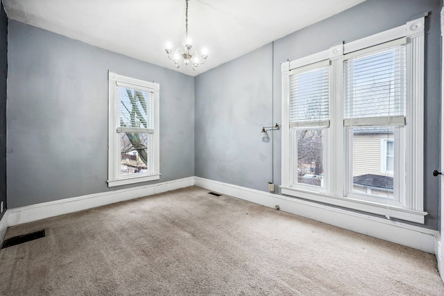 carpeted spare room with an inviting chandelier