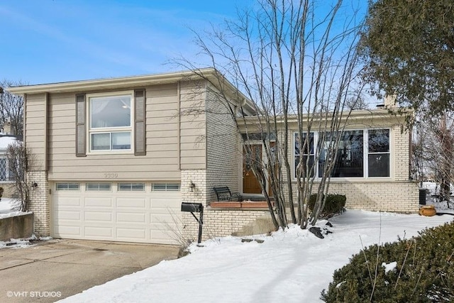 view of snow covered exterior with driveway, brick siding, and an attached garage