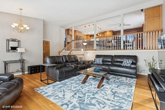 living area featuring ceiling fan with notable chandelier, wood finished floors, baseboards, and stairs