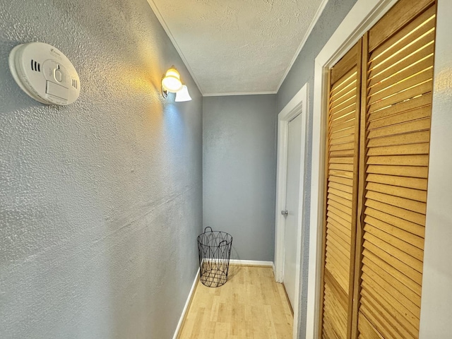 hallway featuring crown molding, light hardwood / wood-style flooring, and a textured ceiling