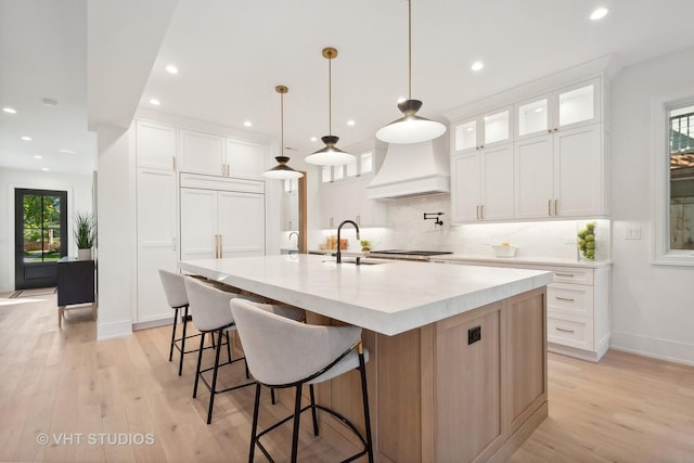 kitchen with hanging light fixtures, white cabinetry, custom range hood, and a large island with sink