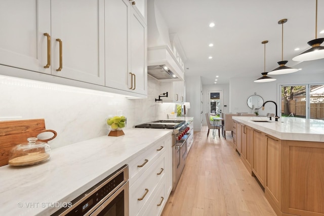 kitchen featuring white cabinets, sink, hanging light fixtures, light stone counters, and custom range hood