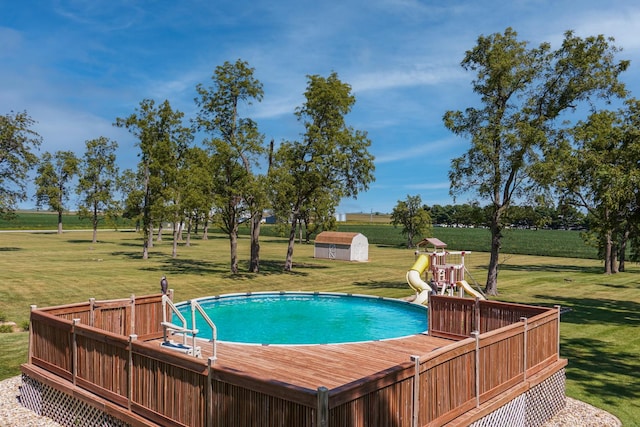 view of pool featuring a yard, a deck, a storage shed, and a playground