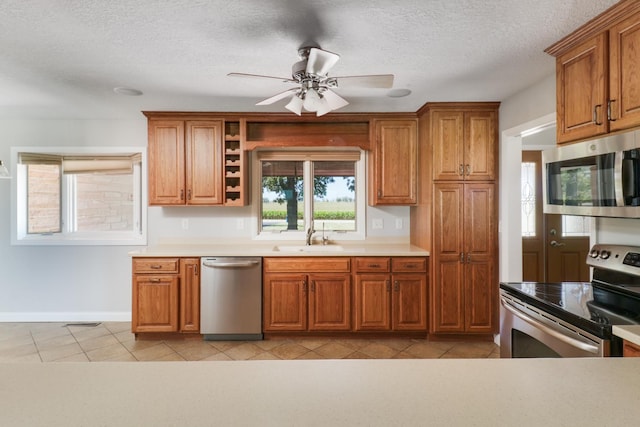 kitchen featuring appliances with stainless steel finishes, sink, light tile patterned floors, a textured ceiling, and ceiling fan