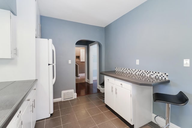 kitchen featuring white cabinetry, decorative backsplash, dark tile patterned floors, and white fridge