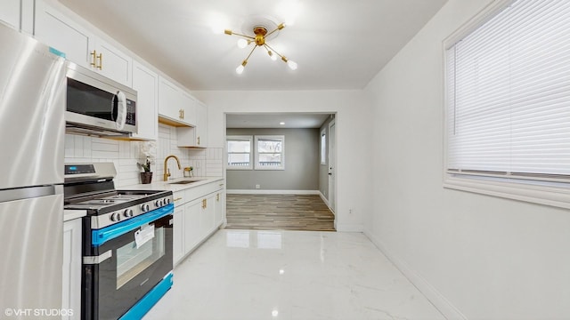 kitchen with backsplash, stainless steel appliances, sink, a chandelier, and white cabinetry