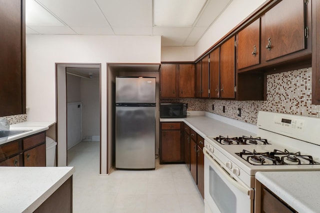 kitchen featuring sink, white gas stove, backsplash, stainless steel fridge, and a drop ceiling