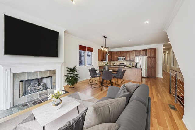 living room with a tiled fireplace, light wood-type flooring, and ornamental molding