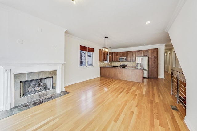 kitchen with stainless steel appliances, a tile fireplace, ornamental molding, light hardwood / wood-style floors, and pendant lighting