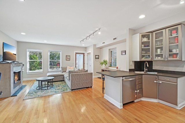 kitchen with sink, rail lighting, stainless steel dishwasher, kitchen peninsula, and light wood-type flooring