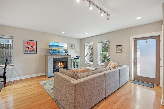 living room with a premium fireplace, rail lighting, and light hardwood / wood-style flooring