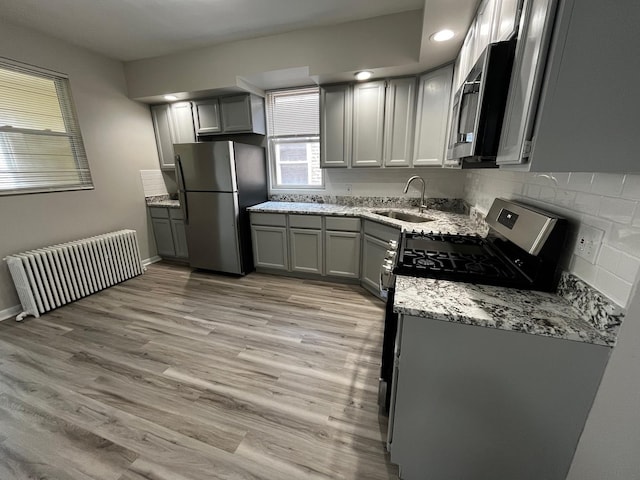 kitchen with sink, stainless steel appliances, radiator heating unit, and gray cabinets