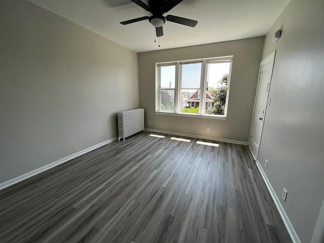 empty room featuring dark hardwood / wood-style flooring, ceiling fan, and radiator heating unit