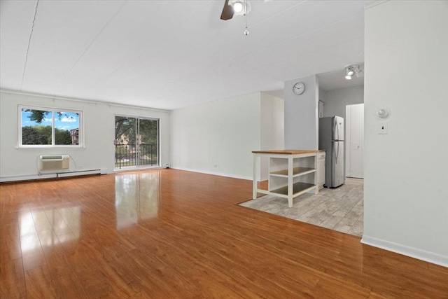 unfurnished living room featuring ceiling fan, light wood-type flooring, a wall unit AC, and a baseboard radiator