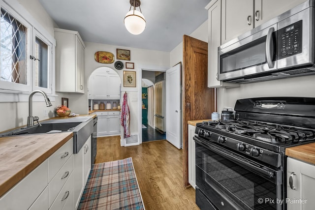 kitchen featuring white cabinets, wood-type flooring, butcher block counters, stainless steel appliances, and sink