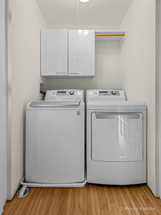 washroom featuring independent washer and dryer, cabinets, and light hardwood / wood-style floors