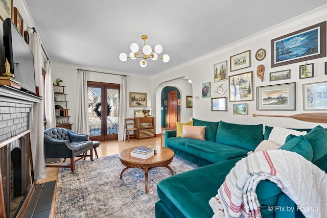 living room featuring crown molding, an inviting chandelier, a fireplace, and french doors