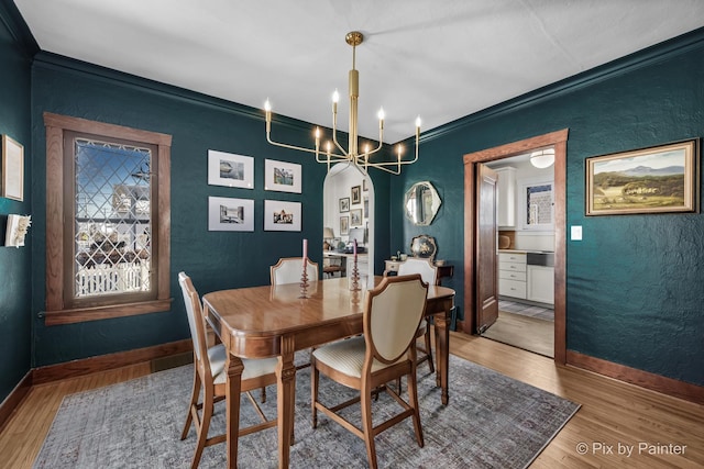 dining area featuring wood-type flooring, a notable chandelier, and crown molding