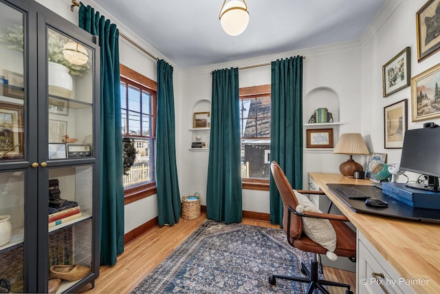 office featuring built in shelves, light wood-type flooring, ornamental molding, and a healthy amount of sunlight