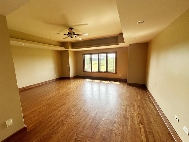 empty room featuring a raised ceiling, ceiling fan, and hardwood / wood-style flooring