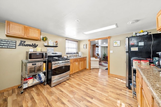 kitchen with stainless steel appliances, light wood-type flooring, light stone counters, light brown cabinets, and sink