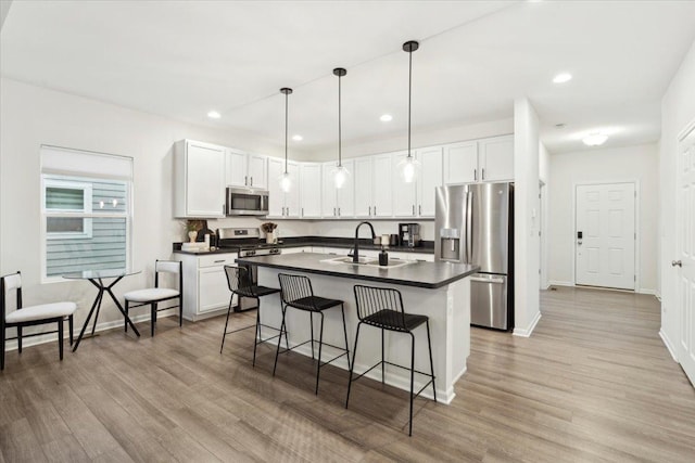 kitchen featuring appliances with stainless steel finishes, decorative light fixtures, a kitchen island with sink, white cabinets, and light wood-type flooring