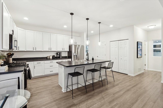 kitchen featuring appliances with stainless steel finishes, a kitchen breakfast bar, pendant lighting, white cabinetry, and an island with sink