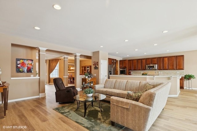 living room featuring recessed lighting, light wood-type flooring, ornate columns, and baseboards