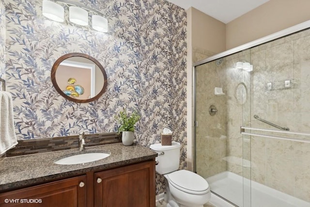 full bathroom with a shower stall, toilet, wallpapered walls, and vanity