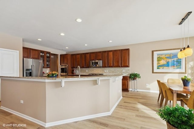 kitchen with light wood-type flooring, a breakfast bar, hanging light fixtures, appliances with stainless steel finishes, and tasteful backsplash