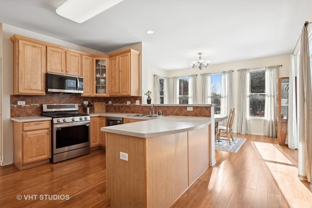 kitchen featuring backsplash, kitchen peninsula, an inviting chandelier, light hardwood / wood-style flooring, and stainless steel appliances