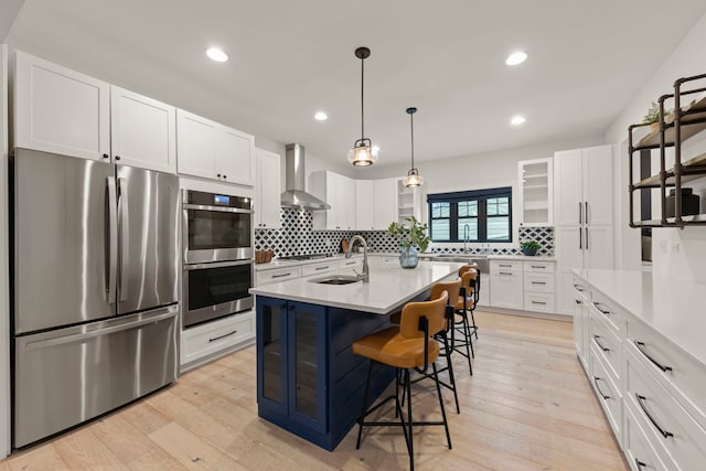 kitchen with wall chimney range hood, sink, appliances with stainless steel finishes, white cabinets, and a center island with sink