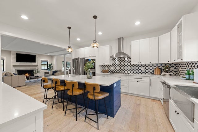 kitchen featuring appliances with stainless steel finishes, a breakfast bar, white cabinetry, an island with sink, and wall chimney exhaust hood