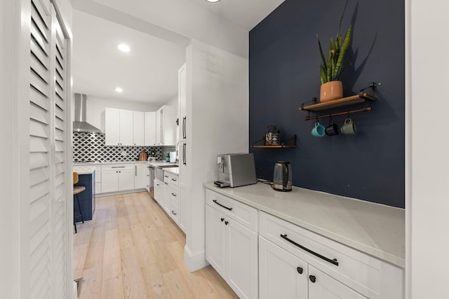 kitchen with tasteful backsplash, wall chimney range hood, white cabinets, and light hardwood / wood-style floors