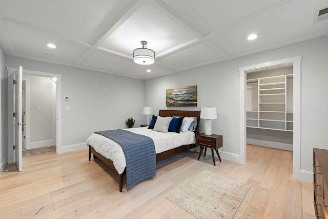 bedroom with coffered ceiling, a spacious closet, light hardwood / wood-style flooring, and a closet