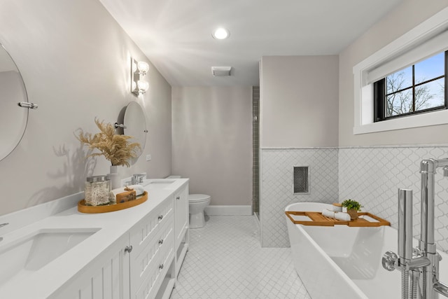 bathroom featuring toilet, tile walls, vanity, tile patterned flooring, and a washtub