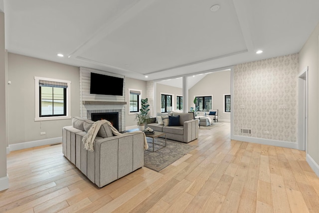 living room featuring a brick fireplace, light hardwood / wood-style flooring, vaulted ceiling, and plenty of natural light