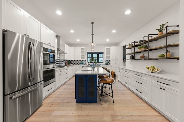 kitchen featuring a breakfast bar, hanging light fixtures, a center island with sink, appliances with stainless steel finishes, and white cabinets