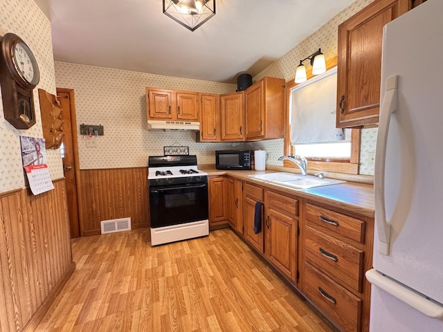 kitchen with wood walls, white refrigerator, sink, light wood-type flooring, and gas stove