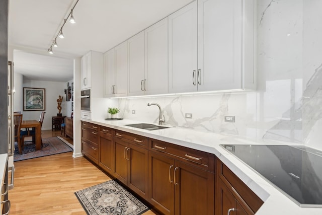 kitchen with decorative backsplash, white cabinetry, sink, and light hardwood / wood-style flooring