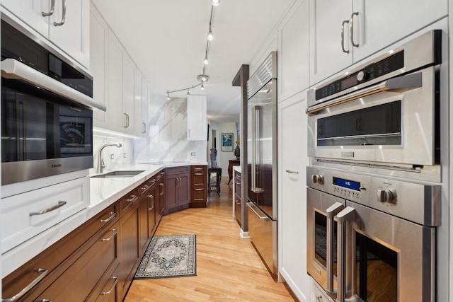 kitchen featuring sink, stainless steel appliances, light hardwood / wood-style flooring, decorative backsplash, and white cabinets