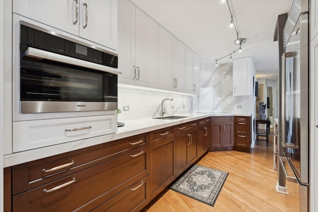 kitchen featuring white cabinets, sink, light hardwood / wood-style flooring, tasteful backsplash, and stainless steel appliances