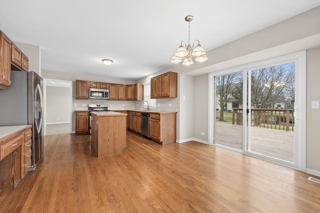 kitchen featuring a healthy amount of sunlight, hanging light fixtures, a notable chandelier, a kitchen island, and appliances with stainless steel finishes